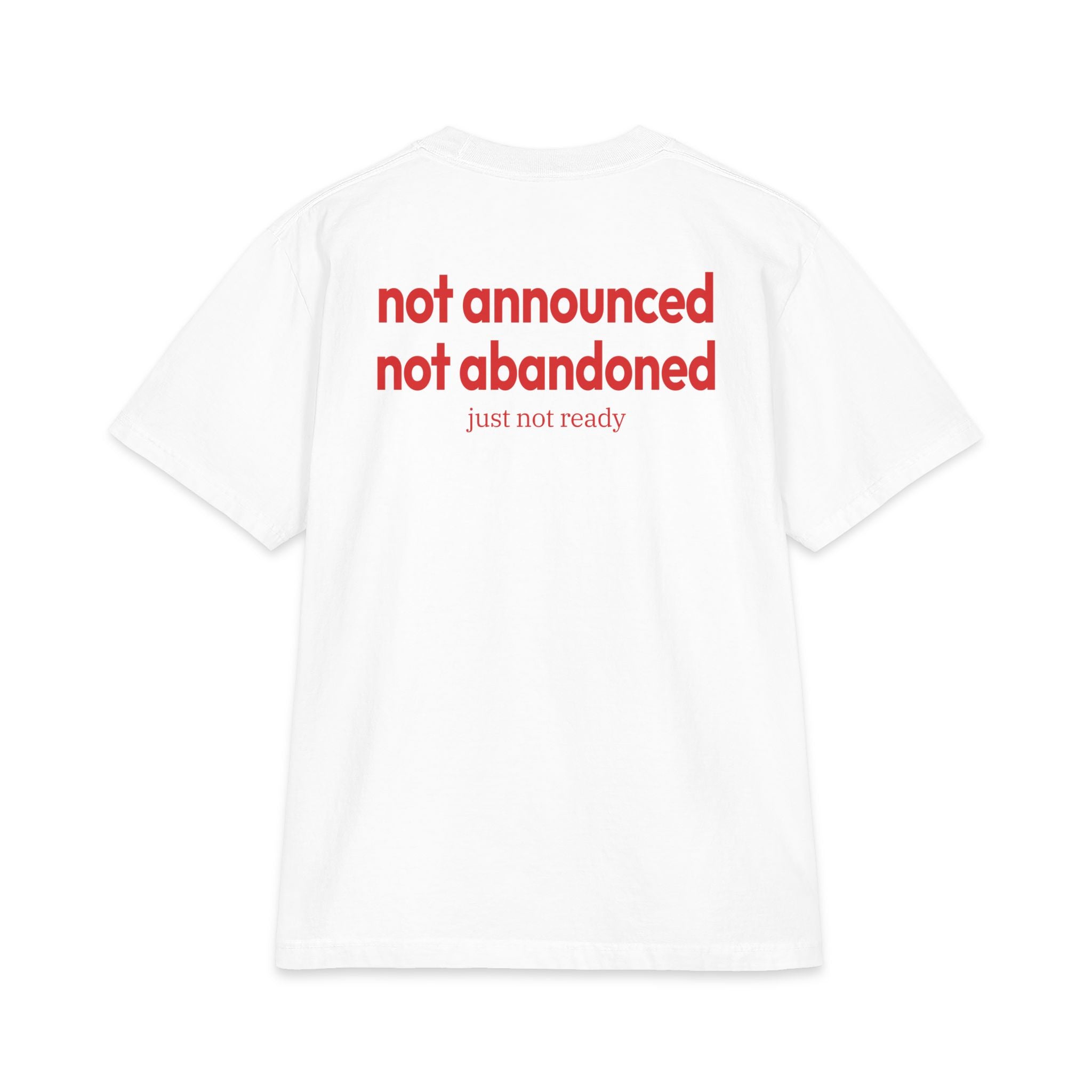 White short-sleeve t-shirt shown from the back, featuring the text 'not announced not abandoned' in red, with 'just not ready' printed below in a smaller red font.