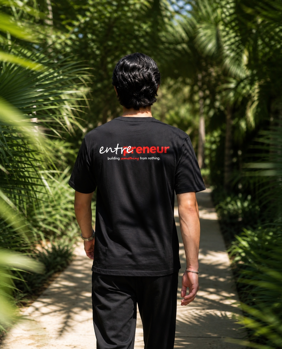 Person wearing a black t-shirt with 'entrepreneur' text, standing in a tropical setting.