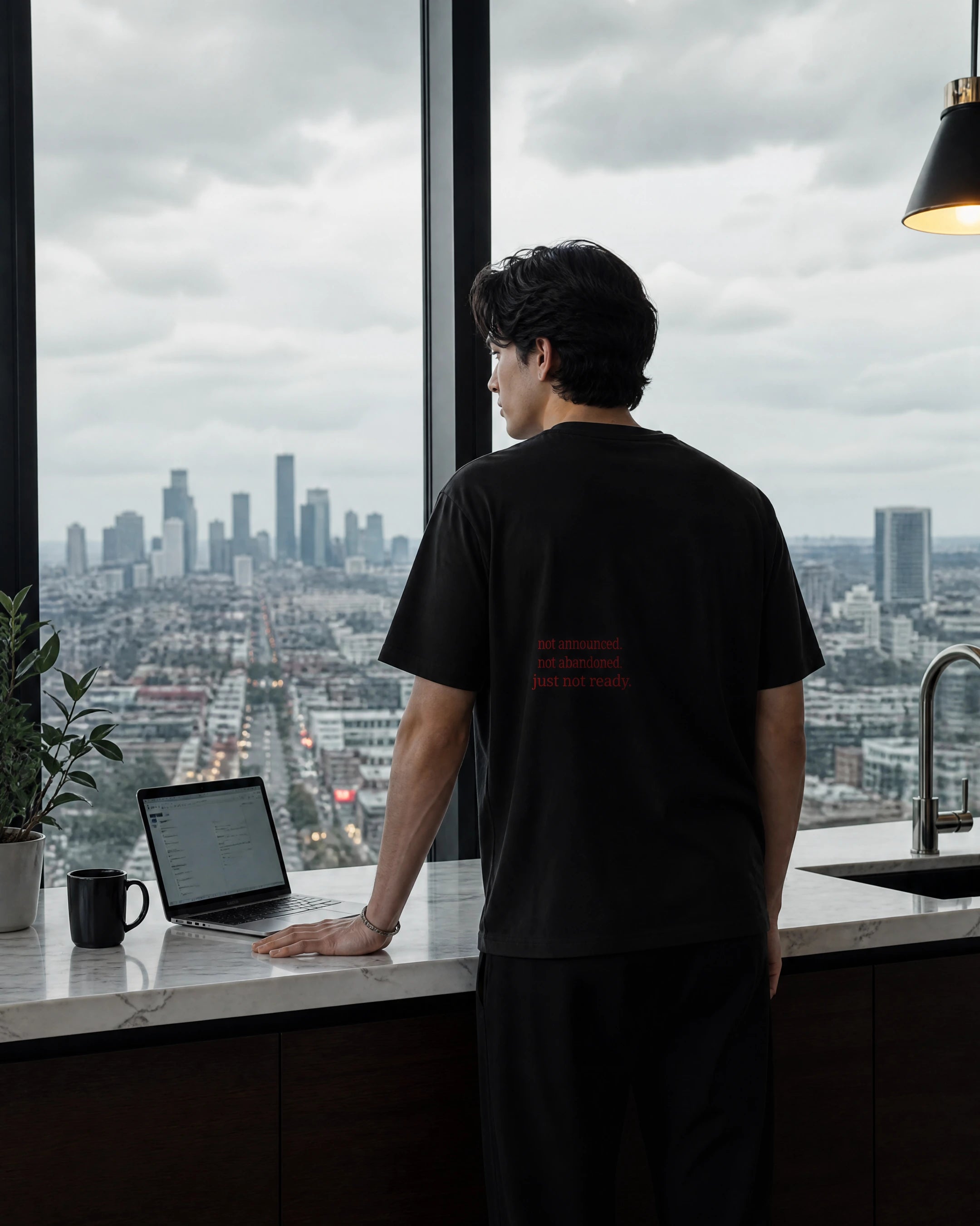 zehran standing in a modern kitchen wearing zeromode quiet tee and looking out at a city skyline