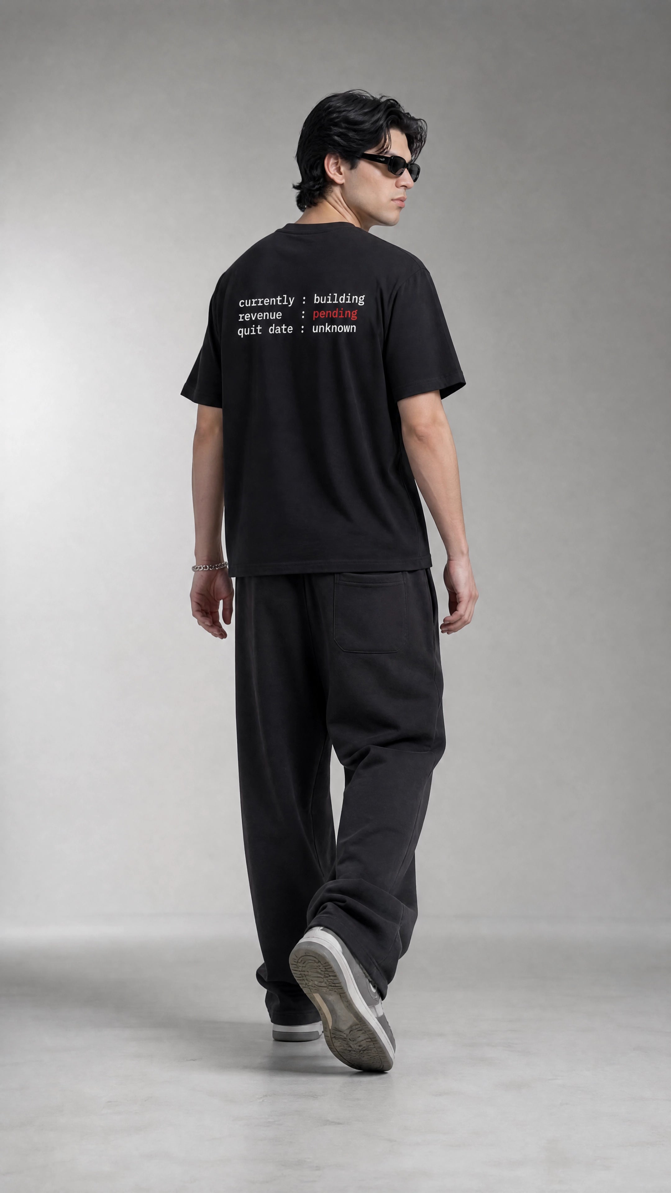 Man wearing a black t-shirt with text and black pants on a gray background